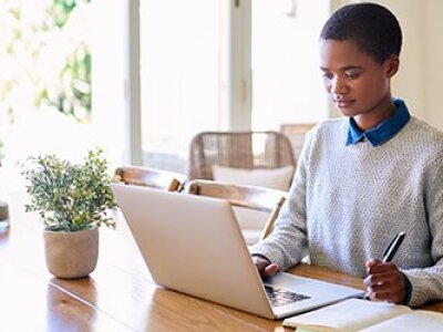 person-in-grey-sweater-blue-collar-sitting-at-wood-table-on-computer-taking-notes
