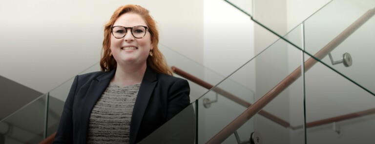 student poses for photo on glass staircase