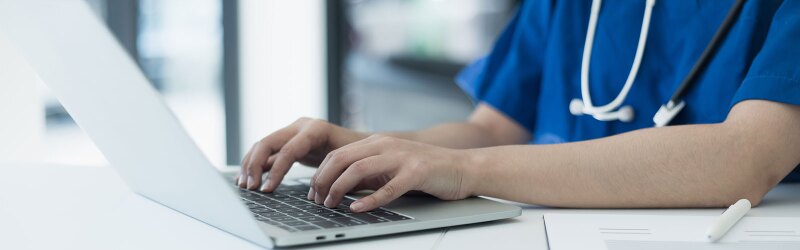A healthcare professional is typing on a laptop, updating medical records, and conducting research.