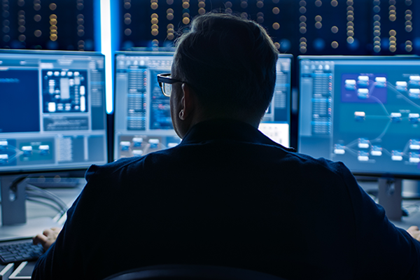 Man in glasses looking at multiple computer screens of data