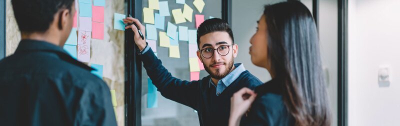 Entrepreneur leads multicultural creative employees collaborating on creating presentation using little sticky papers for writing ideas and productive job.