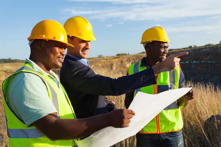 Three surveyors looking at a map and working in a field