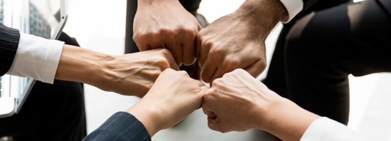 Five people form a circle with their fists for a team fist bump.