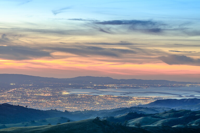 Aerial landscape of mountains and city lights at dusk.