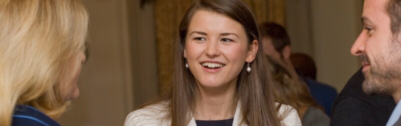 Young woman speaks with another woman and a man at a networking event.