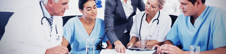 Group of medical professionals seated around table listening to healthcare compliance worker