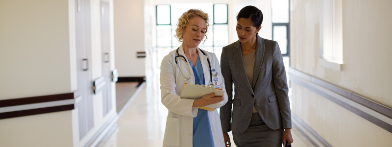 A doctor and hospital administrator walk together in a hospital corridor