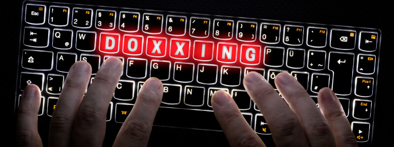 Hands are poised over the keys of a glowing keyboard. The word "doxxing" is highlighted on glowing red keys.
