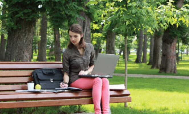 girl sitting on park bench with laptop working