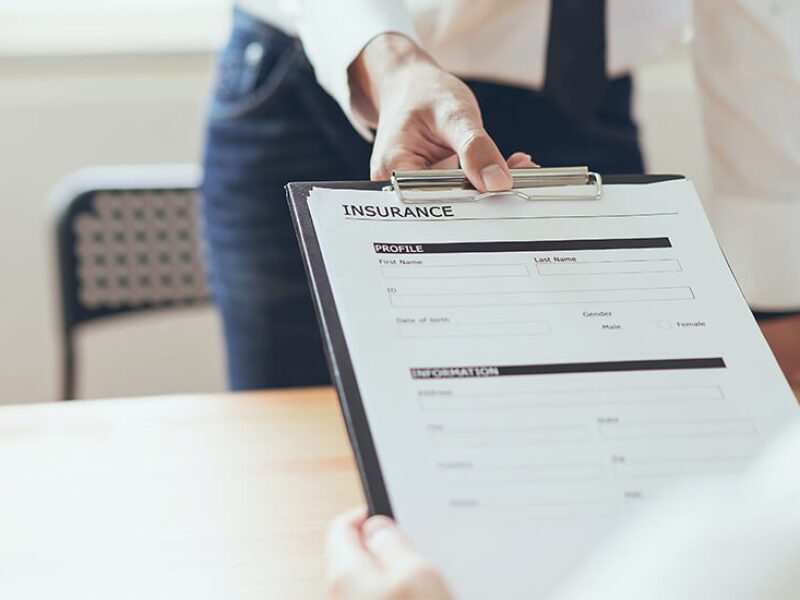 Hand holding insurance forms on clipboard