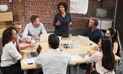 people in a meeting around a table with laptops