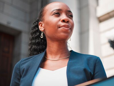 Female lawyer standing outside a law firm looking empowered.