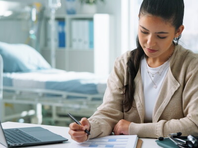 A nurse case manager sits in a hospital room working on paperwork.