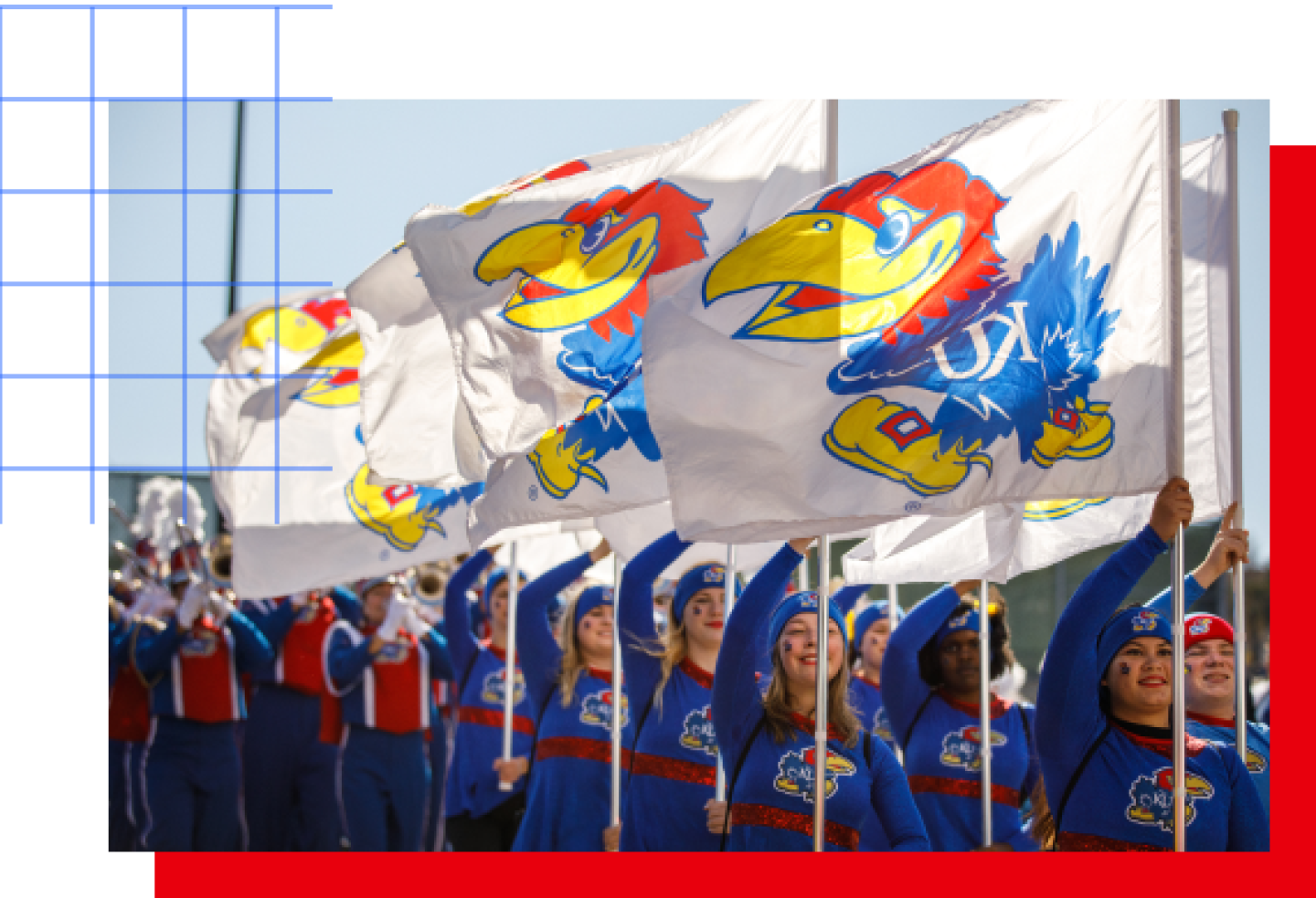 Kansas Jayhawks spirit squad marching outdoors, holding KU flags while a band performs behind them.