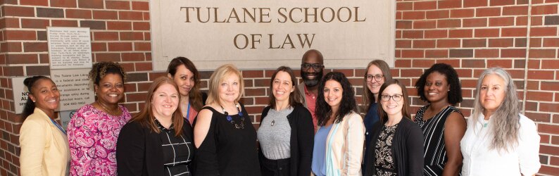 Tulane Law professionals and students stand below the Tulane School of Law sign.