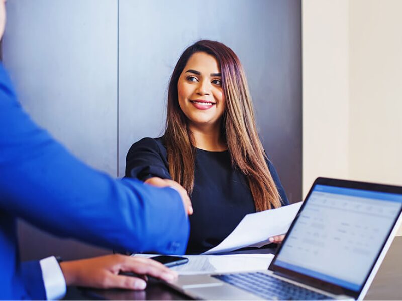 Female corporate compliance officer shaking hands with man at laptop