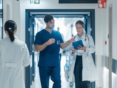 A doctor and a nurse are discussing an upcoming surgery while walking through a busy hospital hallway.