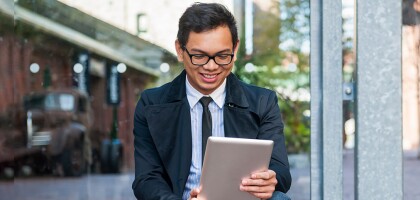 Man in dress clothes outdoors looking at tablet