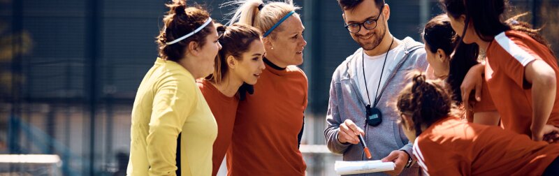 Female players and their coach going through game strategy before soccer match on playing field.