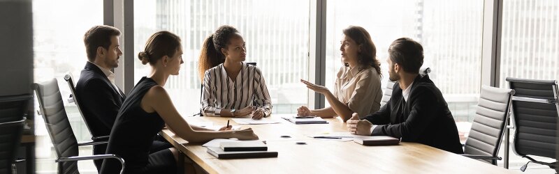 A diverse group of professionals engaged in a discussion around a conference table, representing a collaborative conversation about business ethics and responsible decision-making.