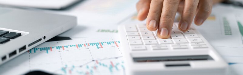 Woman working on desk using a calculator, calculating finances.
