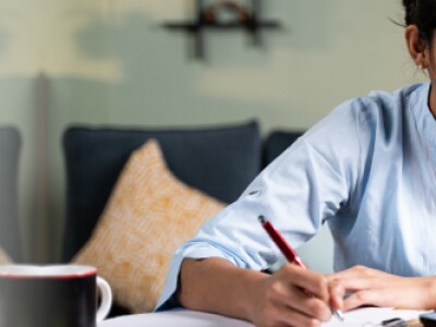 Woman wearing light blue tunic holds pen while looking at a laptop screen in living room