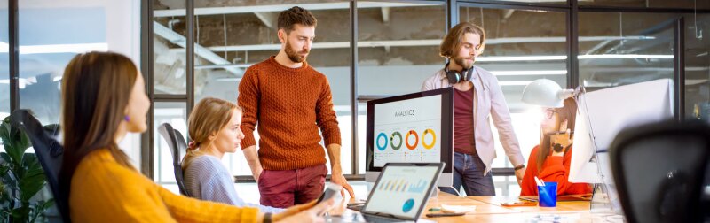 Group of young coworkers dressed casually working together on the computers with some charts sitting in the modern office interior.