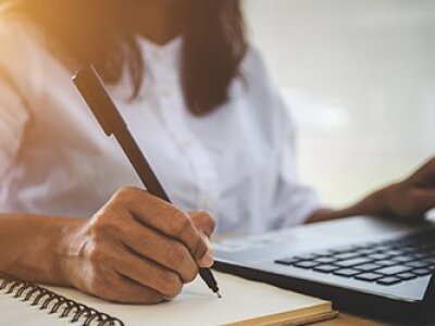 woman-writing-in-notebook-on-laptop-backlit