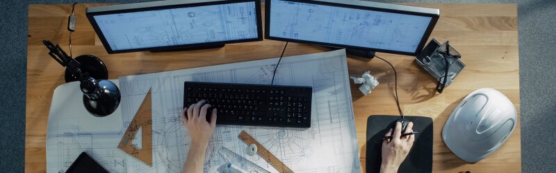 Someone working at a desk with blueprints and a computer.