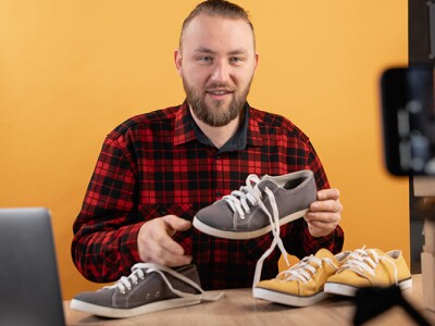 Young bearded vlogger looking at camera reviewing shoes.