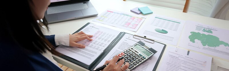 A woman using a calculator while looking at numbers on a piece of paper.