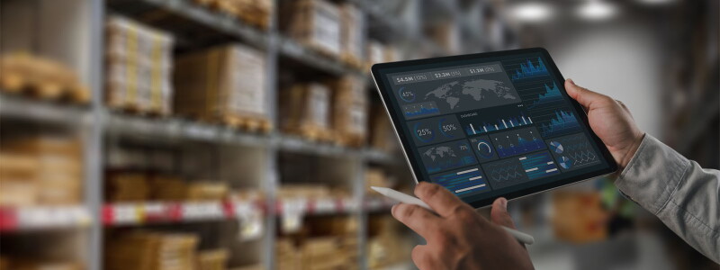 Logistics manager analyzing a supply chain data dashboard on a tablet inside a warehouse facility.
