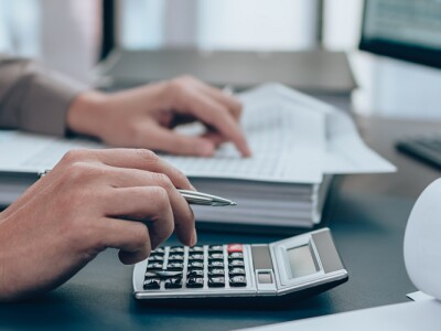 Auditor working at a desk with a stack of spreadsheets and a calculator.