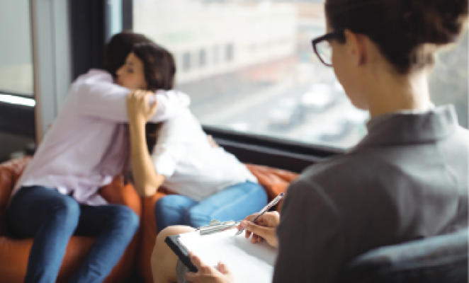 Female therapist with glasses taking notes while patients hug