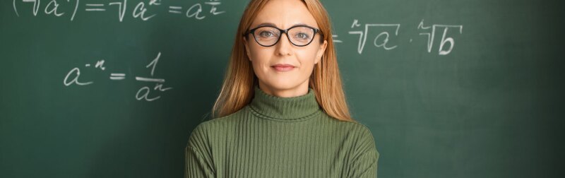 Confident female teacher stands in front of a chalkboard.