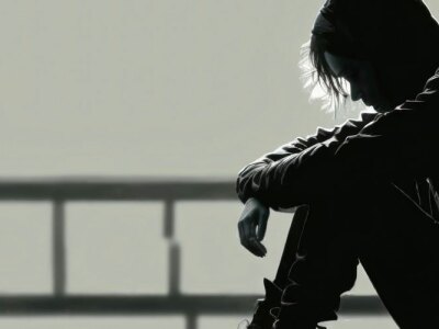 Black and white image of a man sitting on the ground in a hallway with arms crossed.
