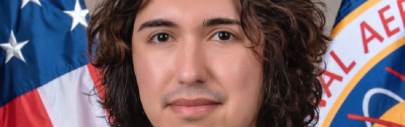 Rudy Ruano standing in front of flags from the USA and NASA