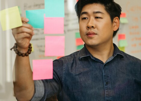 Man in denim dress shirt works with sticky notes on a plexi glass wall