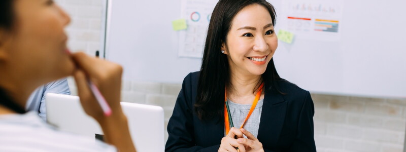 A smiling Asian woman collaborates with teammates in a meeting room.