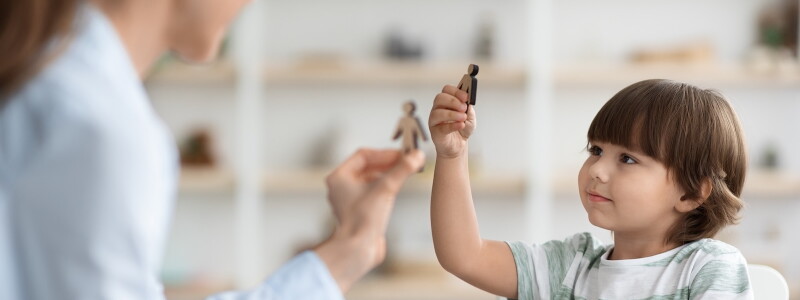 A child and counselor use wooden figures during a play therapy session.
