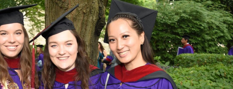 Three IMC graduates smile in their cap and gown