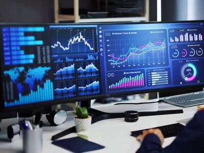A man analyzing data on multiple monitors displaying charts, graphs, and global business metrics in a modern office setting.