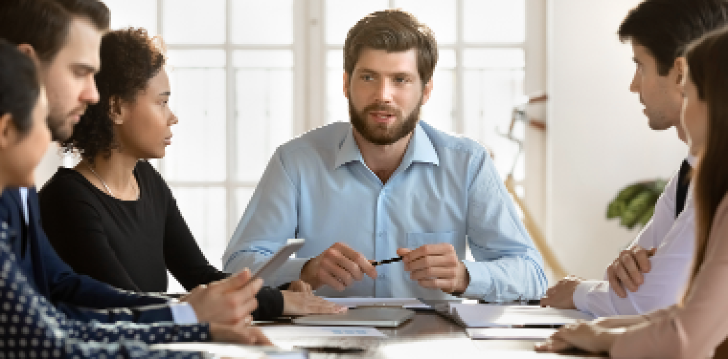 man speaking to a group of people at a table