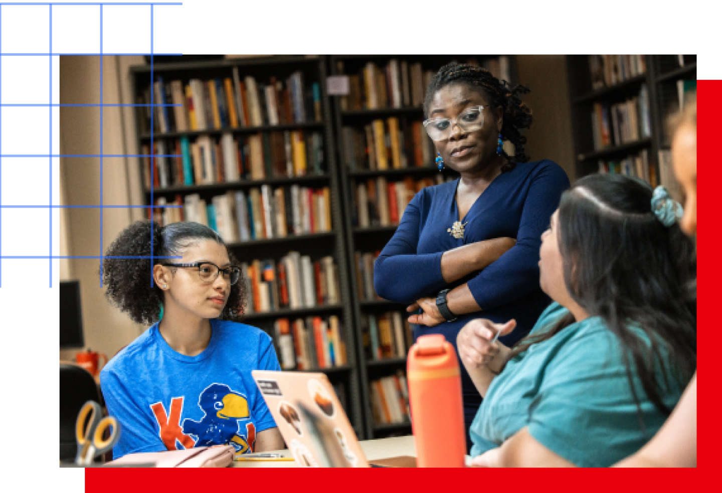 A female KU professor stands with arms crossed while talking with two female KU students.