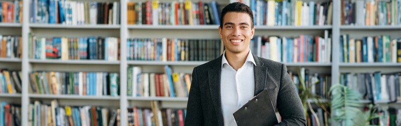 A confident school principal standing in front of a large library bookshelf