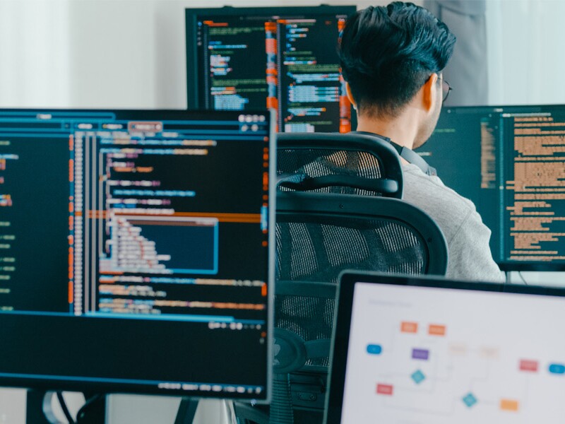 Two workers sit at desks in front of computer screens with data in the displays.