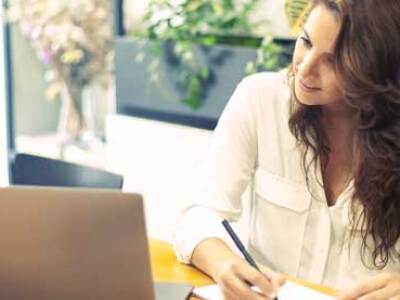 Student taking notes while seated at a laptop