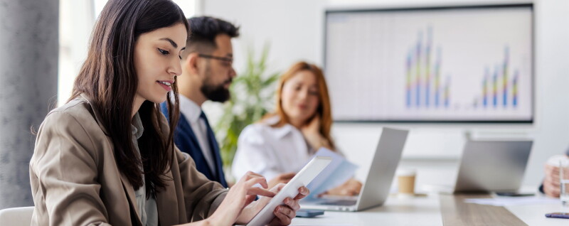 Side view of focused female employee scrolling on tablet while sitting in an office with coworkers.
