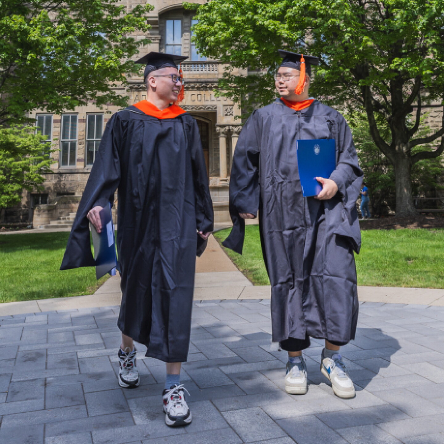 Two male CWRU graduates walking outside the campus grounds.