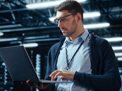 Man working on a laptop in a data center, surrounded by server racks